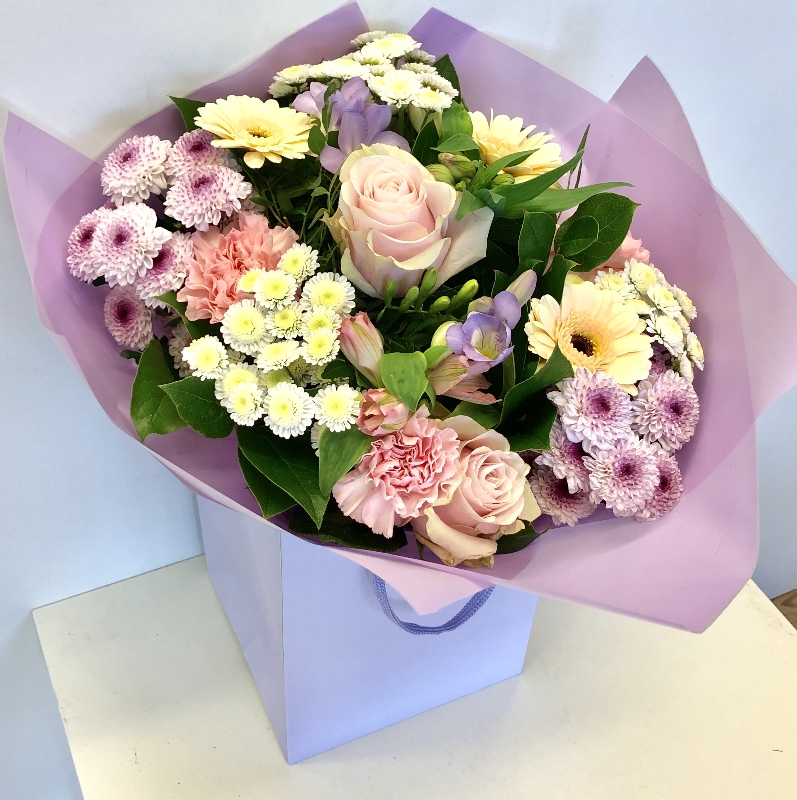 Hand tied bouquet of pastel tones including roses, carnations, chrysanthemums and freesia. 