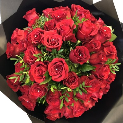 Luxury hand-tied bouquet of 50 large-headed red Freedom roses with sparkling diamanté centres and complementary foliage, wrapped in luxury cellophane and presented in a signature black gift bag with rope handles.