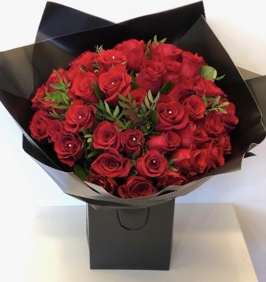 Luxury hand-tied bouquet of 50 large-headed red Freedom roses with sparkling diamanté centres and complementary foliage, wrapped in luxury cellophane and presented in a signature black gift bag with rope handles.