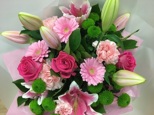 Luxurious bouquet featuring pink roses, pink lilies, pink germini, and lime green chrysanthemums, elegantly wrapped in premium cellophane with a matching gift bag.