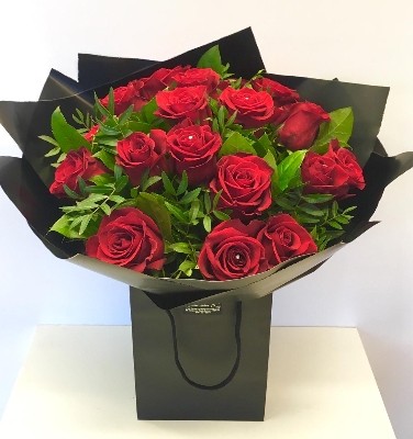 Eighteen luxury red Freedom roses, hand-tied in water, wrapped in modern cellophane, and presented in a signature black gift bag, with diamante rose centres for added sparkle.