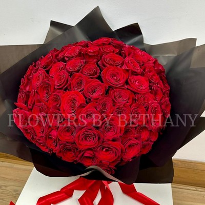Hand-tied bouquet of 100 luxury large-headed red Freedom roses, wrapped in frosted black cellophane with a large red satin ribbon, and delivered with a FREE XL glass vase. Size: 24 x 24 Inch.