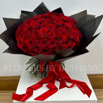 Hand-tied bouquet of 100 luxury large-headed red Freedom roses, wrapped in frosted black cellophane with a large red satin ribbon, and delivered with a FREE XL glass vase. Size: 24 x 24 Inch.