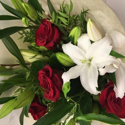Hand-tied bouquet featuring luxury red Freedom roses, white lilies, and willow accents, wrapped in luxury cellophane and matching gift bag, hand-tied in water.