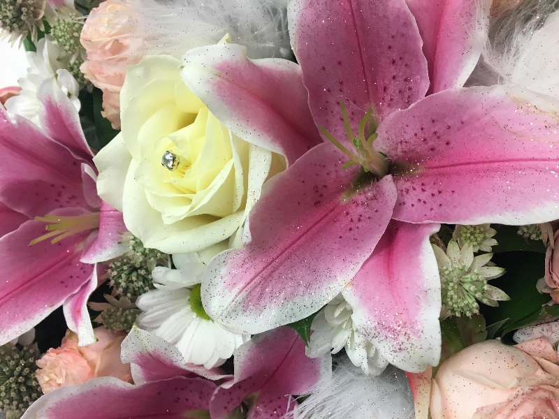 Mixed floral heart with lily, roses and chrysanthemum finished with white feathers, diamantes and glitter dusting. 
