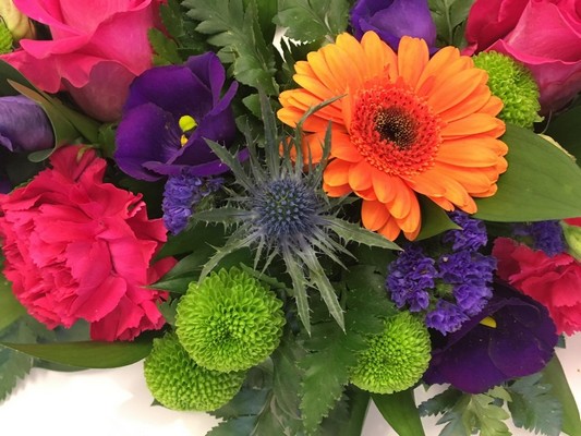 Vibrant funeral wreath with cerise, orange, purple, and lime green flowers on a rich green foliage base.