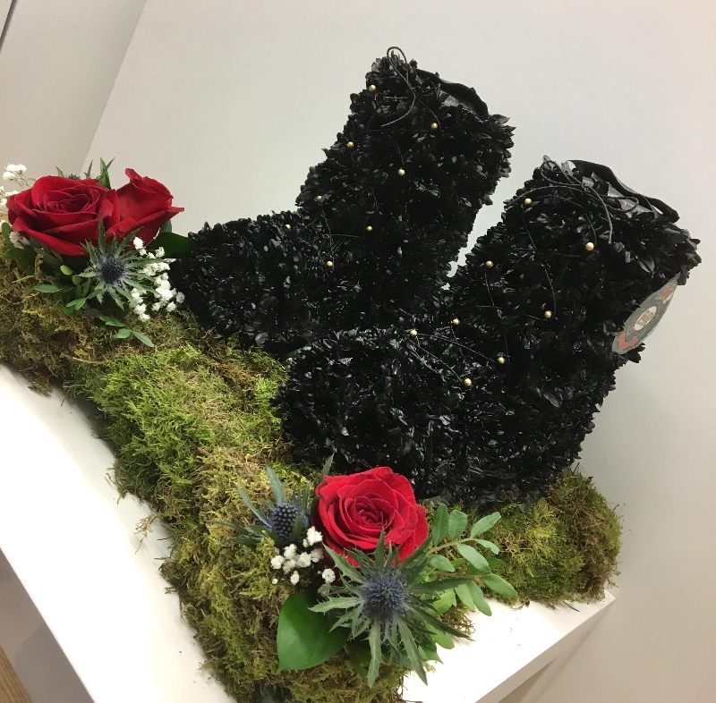 Black army boots funeral tribute with moss base and gold buckle detailing. 