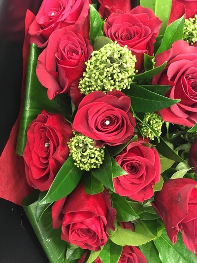 Luxury bouquet featuring large-headed red roses, skimmia, aspidistra folded leaves, and diamanté centres, wrapped in luxury cellophane and presented in a matching hat box, hand-tied in water.