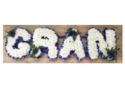 GRAN lettering, massed with white chrysanthemum and dark blue ribbon edging. 