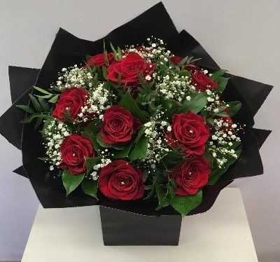 Twelve luxury red roses with white gypsophila, accented with complementary foliage, wrapped in luxury cellophane and matching gift bag, hand-tied in water.