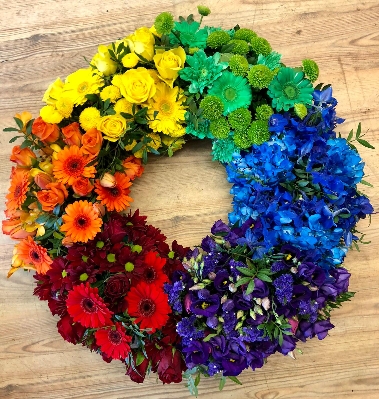 Beautiful rainbow wreath created by making segments of the rainbow in seasonal flowers. 