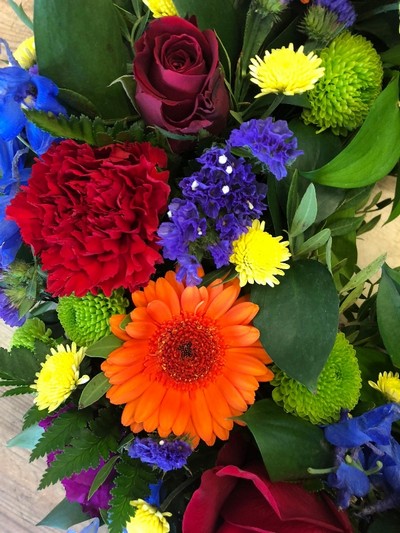 Elegant funeral wreath with vibrant flowers in orange, red, blue, purple, green, and yellow, accented with lush foliage.