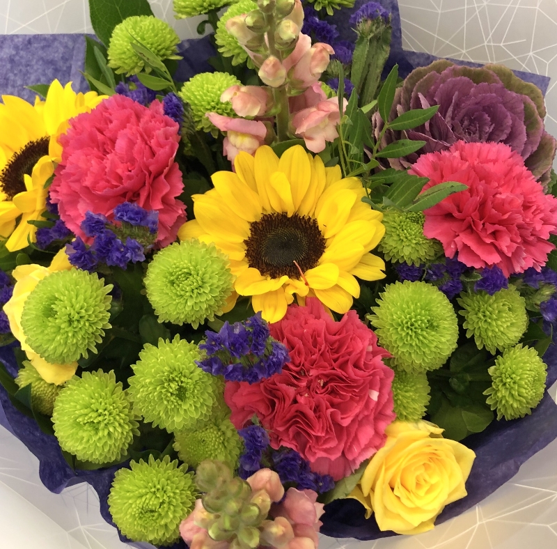 Hand tied bouquet in water with a vivid mix of colour including roses, carnation, chrysanthemums and brassica. 