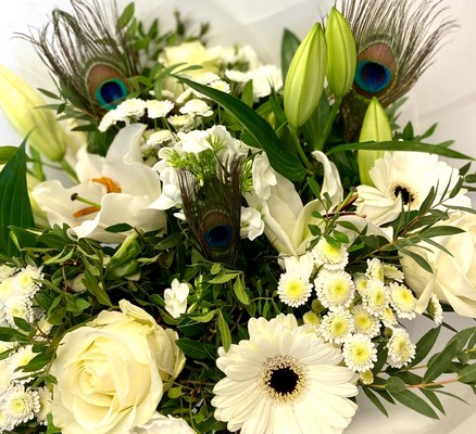 Elegant white bouquet featuring lilies, roses, alstroemeria, and chrysanthemums, accented with vibrant peacock feathers and presented in a luxury hatbox.