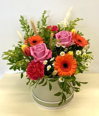 Arrangement design that includes vivid tones of roses, germini and daisy's finished with corn and pampas grass in a luxury hat box. 