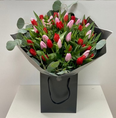 Bouquet of mixed red and pink tulips, accented with foliage and loose populous eucalyptus, wrapped in luxury cellophane and presented in a matching gift bag, hand-tied in water.