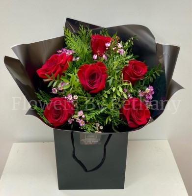 Bouquet featuring 6 luxury red roses with pink wax flowers, accented with diamanté in the roses, complemented by foliage, wrapped in luxury cellophane and matching gift bag, hand-tied in water.