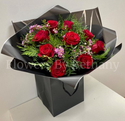Bouquet of nine luxury red Freedom roses with pink wax flowers, accented with diamanté and complementary foliage, wrapped in luxury cellophane and matching gift bag, hand-tied in water.