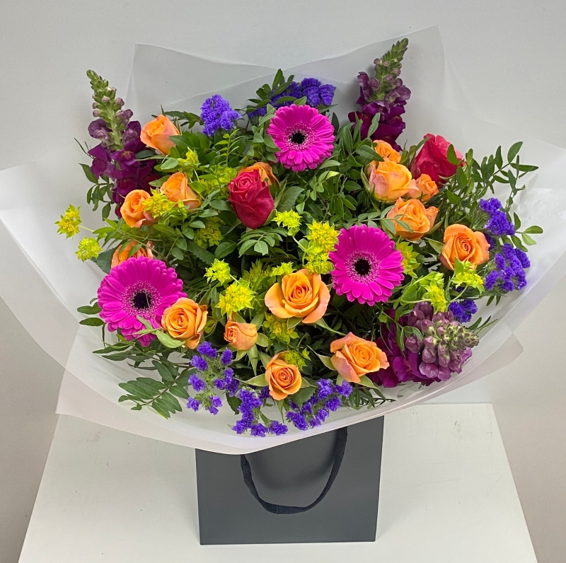 Hand tied bouquet in water including cerise germini, orange spray rose and purple snapdragons. 