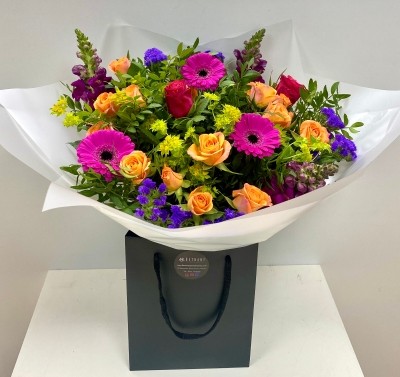 Hand tied bouquet in water including cerise germini, orange spray rose and purple snapdragons. 