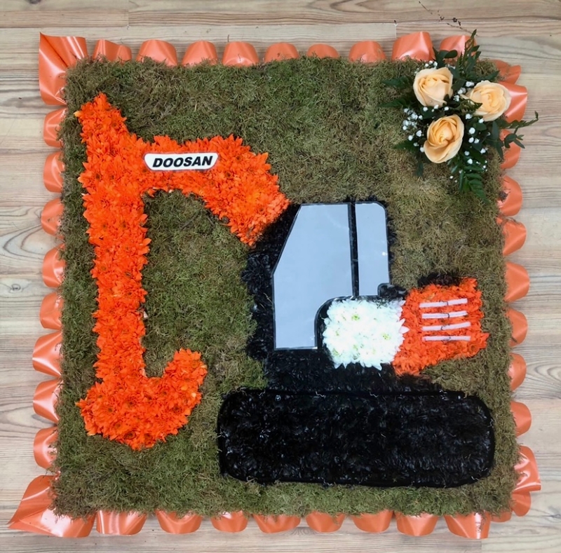 Doosan digger funeral tribute with vivid orange chrysanthemum on a moss board and finished with printed detailing. 