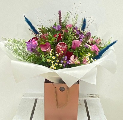 Hand tied bouquet boasting ruby red's, tanzanite and amethyst tones including roses, calla lily and clematis. 