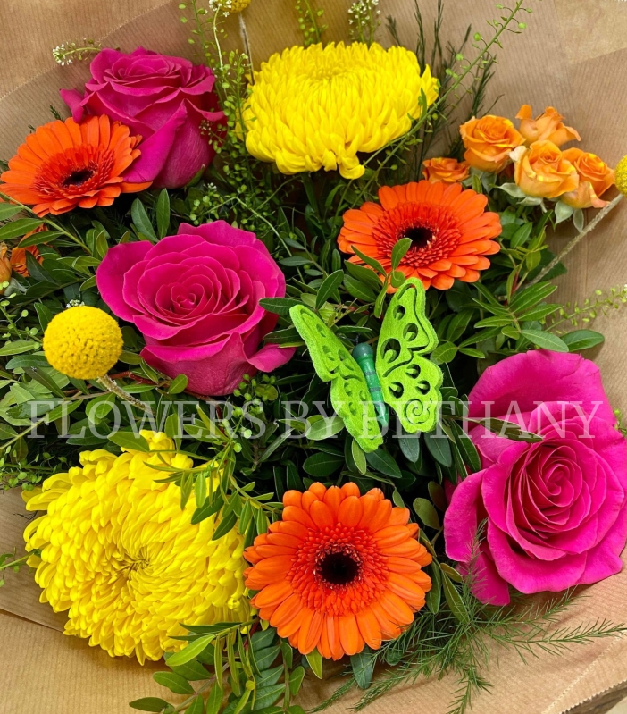 A bright bouquet in orange, yellow and cerise. Including roses, germini, spray rose, green bell and more. Presented in a kraft bag and wrap. 