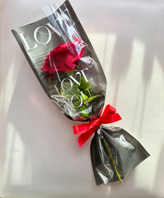 A single red rose elegantly cradled in a paper wrap adorned with heartfelt words of love.