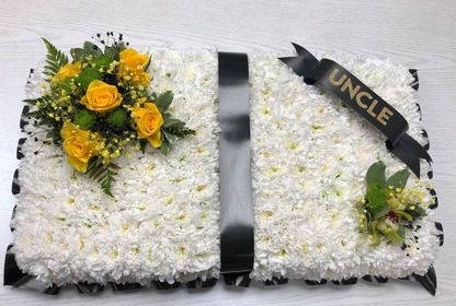 Open prayer book funeral tribute with yellow focal flowers.