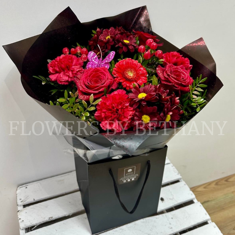Gift bouquet in water including large red roses and red carnations finished with glitter and butterflies. 