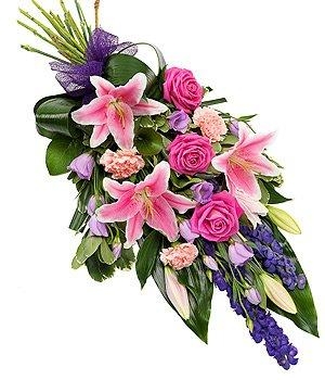 Pink rose and lily hand-tied flat spray with lisianthus, carnations, and aspidistra leaves, finished with a bow.