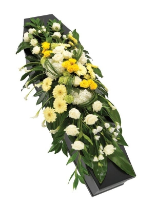 White and yellow casket spray with grouped seasonal blooms, deep green foliage, and grass.