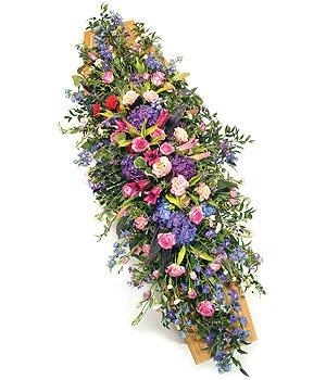Natural casket spray with pink, purple, blue, and lilac seasonal blooms in a luxury garden-style design.