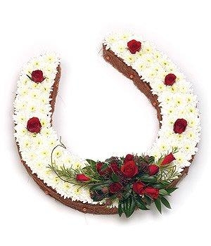 Horse shoe funeral tribute in white with red focal flowers. 