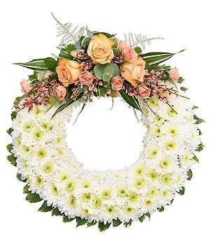Massed white chrysanthemum funeral wreath with peachy pink focal point. 