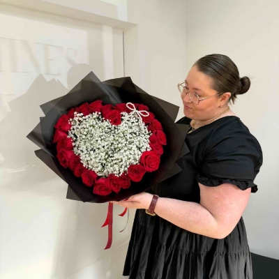 Valentine’s bouquet made with 24 premium red roses arranged around a white gypsophila heart with a pearl bow, wrapped in black with red ribbon, designed out of water with options for a gift bag with water bubble or upgrade to a modern glass vase.