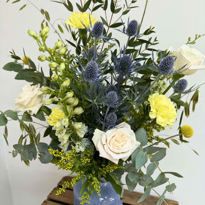 Highland Meadow vase arrangement featuring seasonal ivory, yellow and blue-toned florals with natural meadow-style movement, arranged in a blue ceramic vase by Flowers by Bethany.