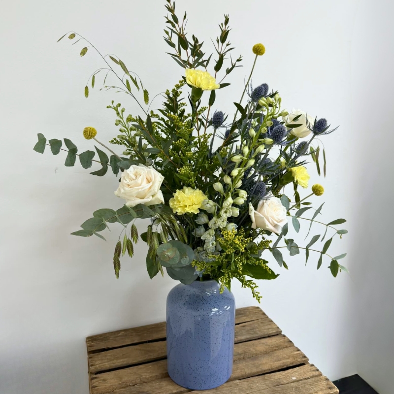 Highland Meadow vase arrangement featuring seasonal ivory, yellow and blue-toned florals with natural meadow-style movement, arranged in a blue ceramic vase by Flowers by Bethany.