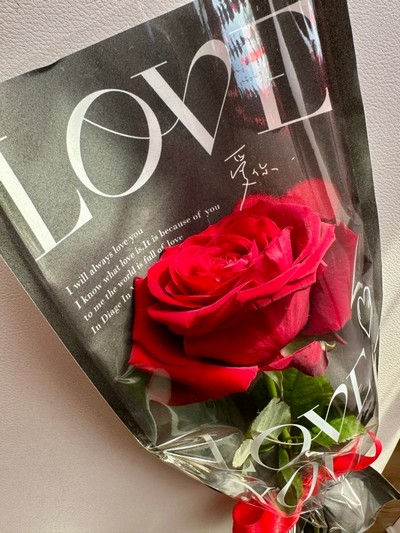 A single red rose elegantly cradled in a paper wrap adorned with heartfelt words of love.