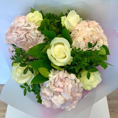 Hand tied bouquet of soft pink hydrangea and white roses, wrapped in luxury cellophane and a gift bag. 