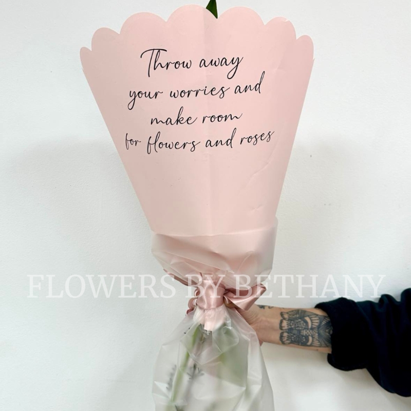 A petite hand tied bouquet in mixed pink hues in a pink scalloped wrap with positivity script. 