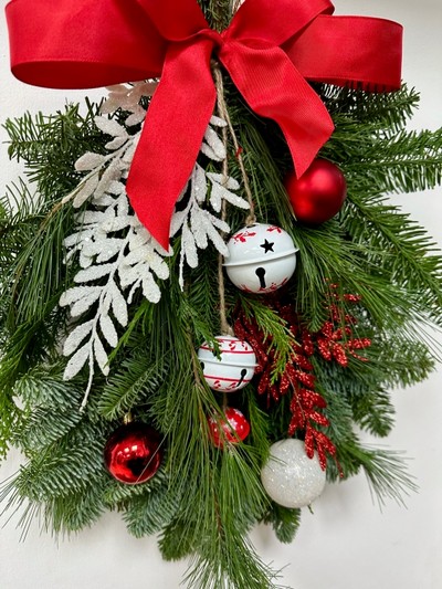 Red and white door swag, a bundle of winter foliage decorated with baubles, glitter foliage, bells and a red bow. 