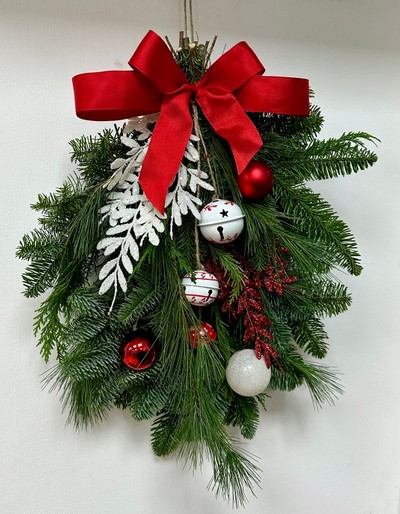 Red and white door swag, a bundle of winter foliage decorated with baubles, glitter foliage, bells and a red bow. 