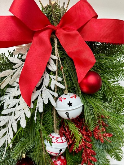 Red and white door swag, a bundle of winter foliage decorated with baubles, glitter foliage, bells and a red bow. 