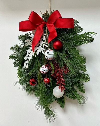 Red and white door swag, a bundle of winter foliage decorated with baubles, glitter foliage, bells and a red bow. 