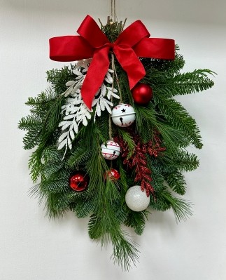 Red and white door swag, a bundle of winter foliage decorated with baubles, glitter foliage, bells and a red bow. 
