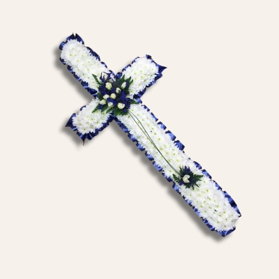 White chrysanthemum funeral cross with blue ribbon edging and blue and white flower spray, accented with mixed foliage.