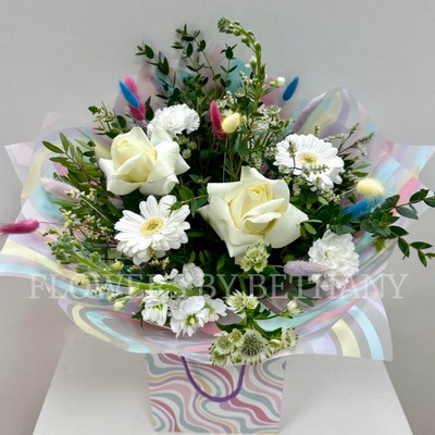 All white bouquet with a whimsical twist, pastel bunny tails dispersed through the bouquet. Wrapped in a wavy print bag and cellophane hand tied in water. 