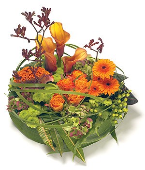 Modern funeral posy with orange, gold, and green seasonal flowers, wrapped in grasses, leaves, and mixed foliage for a contemporary look.