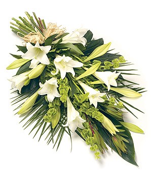 Lilies and Bells of Ireland funeral spray with foliage and a raffia bow.